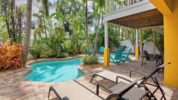 A pool area with lounge chairs, a covered seating area, and surrounding tropical vegetation. - 5 Min Walk to Beach | Private Pool | AMI Trolley (Holmes Beach)