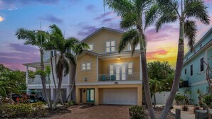 A two-story residential building with a garage, surrounded by palm trees and a driveway. - 5 Min Walk to Beach | Private Pool | AMI Trolley (Holmes Beach)