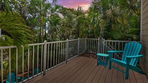 A wooden deck with a white railing, surrounded by lush tropical vegetation, and two turquoise Adirondack chairs. - 5 Min Walk to Beach | Private Pool | AMI Trolley (Holmes Beach)