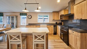 A kitchen with wooden cabinets, a central island with chairs, a stove, and a microwave. - Host Stay Sandy Lane Lodge (York)