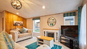 A cozy living room with a sofa, coffee table, TV, fireplace, and a painting on the wall. - Host Stay Sandy Lane Lodge (York)