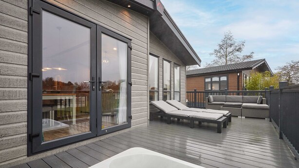A deck with a hot tub, lounge chairs, and a sliding glass door leading to a patio. - Host Stay Sandy Lane Lodge (York)