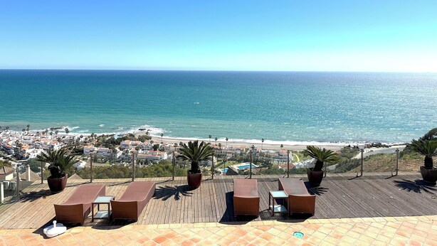 Zeezicht vanaf een dak terras met lounge stoelen, plantenbakken en een helder uitzicht op de oceaan en het strand.