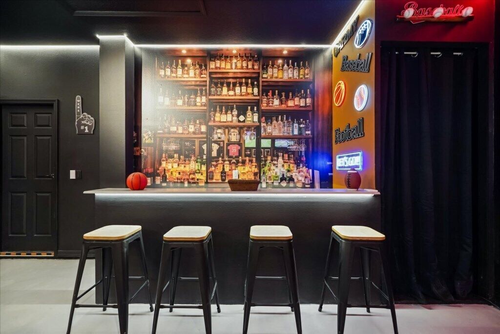 Un espace bar avec des tabourets, des étagères remplies de bouteilles et un panneau lumineux au néon.