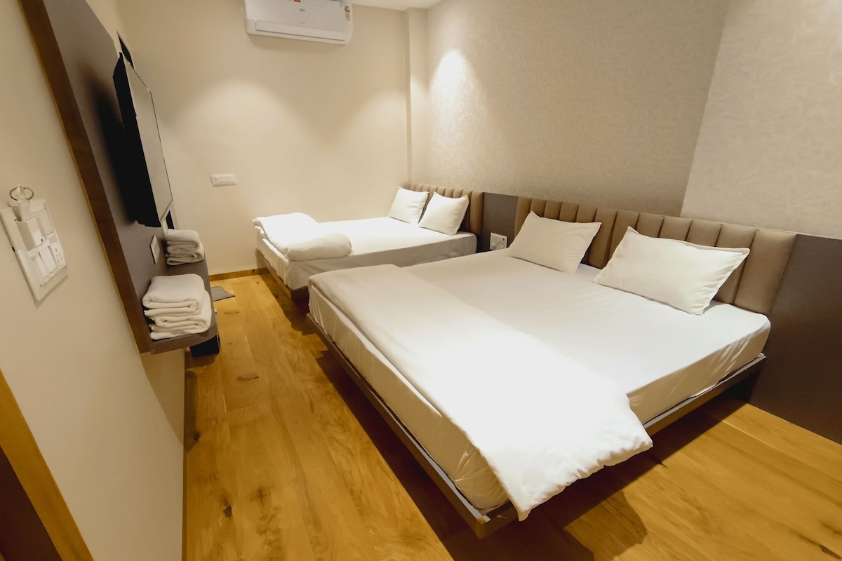 A hotel room with two beds, a wooden floor, a wall-mounted air conditioner, and a small table with towels.