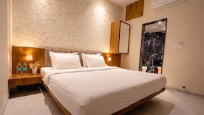 A modern hotel room with a large bed, two bedside tables with lamps, a wall-mounted air conditioner, and a large mirror. - Rukkmannie Holiday Inn (Ujjain)