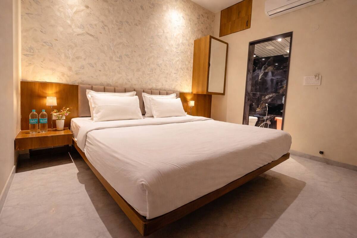 A modern hotel room with a large bed, two bedside tables with lamps, a wall-mounted air conditioner, and a large mirror.