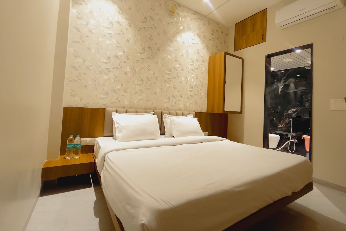 A hotel room with a bed, a nightstand, a wall-mounted mirror, and an air conditioning unit.