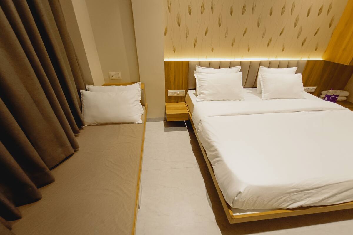 A hotel room with a large bed, a bedside table, a nightstand, and a curtain.