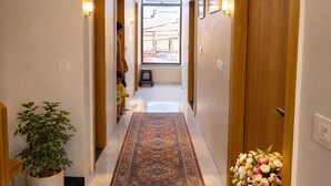 A hallway with a patterned carpet, wooden doors, and a potted plant. - Rukkmannie Holiday Inn (Ujjain)