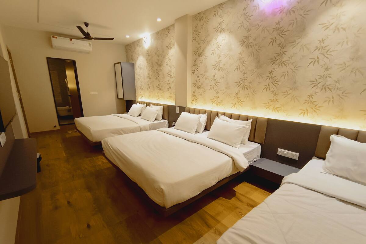 A hotel room with three beds, a wooden floor, a ceiling fan, and a wall with a bamboo pattern.
