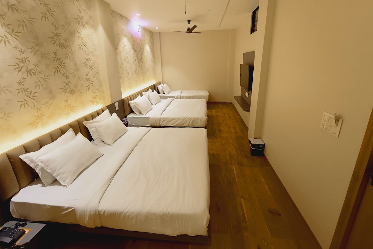 A hotel room with three beds, a ceiling fan, a TV, and a wooden floor.