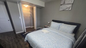 Ett sovrum med en säng, ett nattduksbord, en lampa, en garderob och en dörr som leder till ett annat rum.