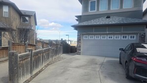 En uppfart till ett bostadshus med ett garage, en parkerad bil och ett trästaket.