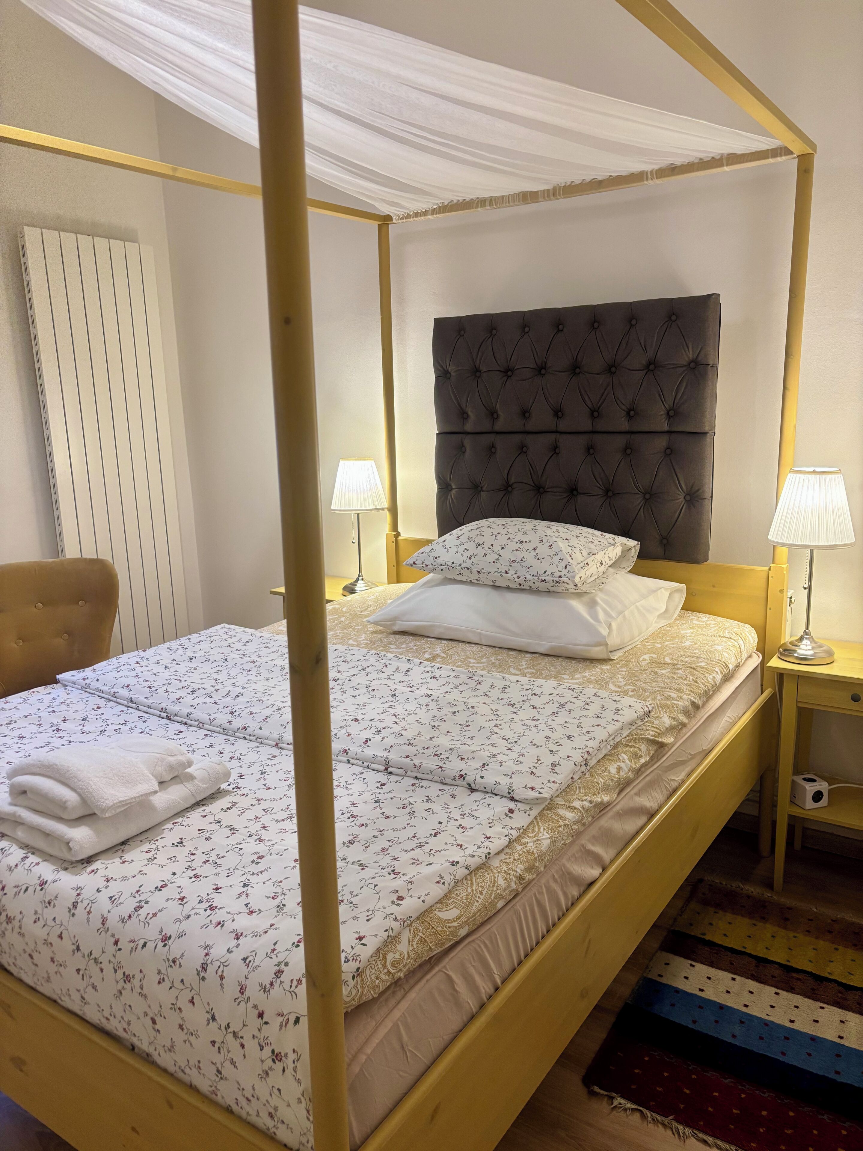 Ein Bett mit Baldachin, dessen Kopfteil mit Knöpfen verziert ist, weiße blumige Bettwäsche und ein Satz weißer Handtücher.