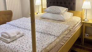 A four-poster bed with a tufted headboard, white floral bedding, and a set of white towels. - Emma Apartments - Studio apartment for 1 guest (Hlavní město Praha)