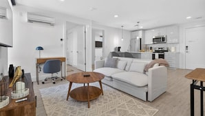 A modern living room with a sofa, coffee table, and a desk with a lamp. - Luxury 2BR | Free Parking | Harvard/BU | ROKU TV (Boston)