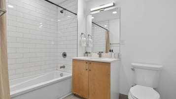 A bathroom with a white bathtub, wooden vanity, and a toilet.