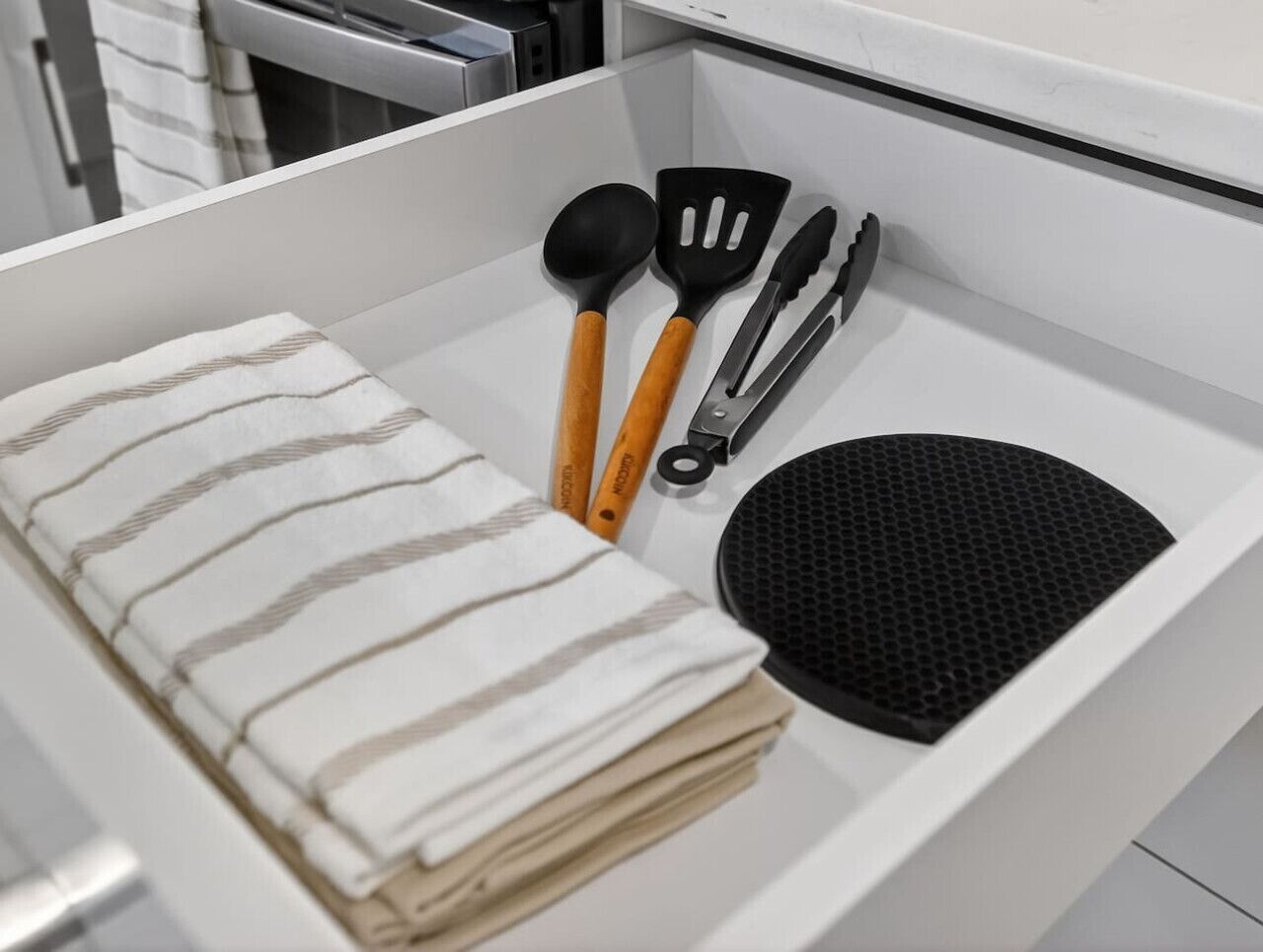 A kitchen drawer containing a striped cloth, a black spatula, a black spoon, and a black grater.