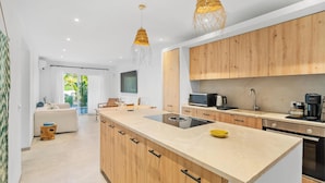 A modern kitchen with wooden cabinets, a central island, and pendant lighting. - Fantastic garden apartment directly on the dream beach of Puerto Alcudia (Alcúdia)
