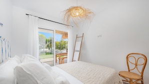 A bedroom with a bed, a chair, a table, and a view of the outdoors. - Fantastic garden apartment directly on the dream beach of Puerto Alcudia (Alcúdia)
