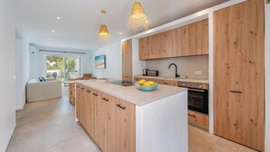 A modern kitchen with wooden cabinets, a central island, and pendant lighting. - Fantastic garden apartment directly on the dream beach of Puerto Alcudia (Alcúdia)