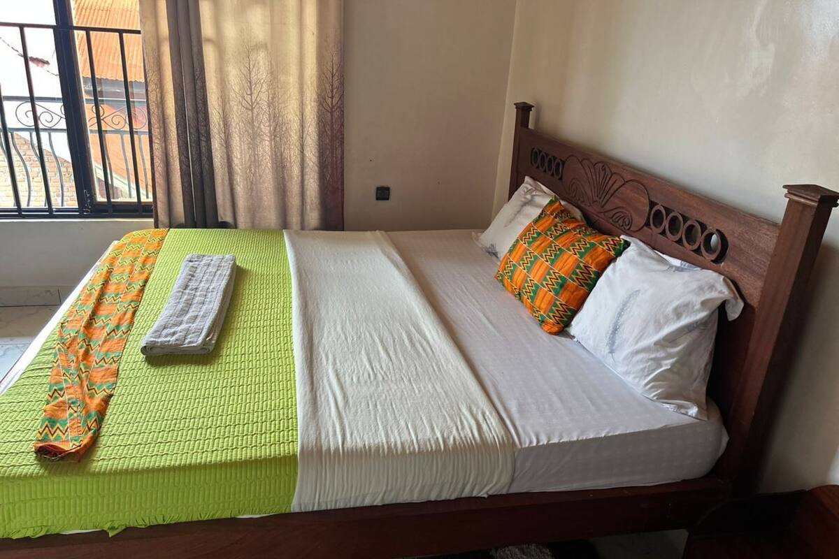 A bed with a green and white bedspread, a patterned blanket, and a pillow with a geometric design.