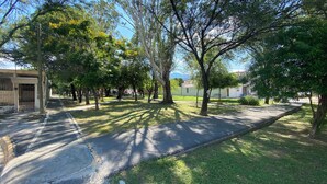 Un camí pavimentat flanquejat per arbres i una zona verda, que condueix a un edifici amb entrada tancada per una reixa.