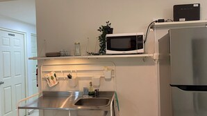 Cuina compacta amb microones, nevera, rentapelats i una petita estant amb una planta i alguns pots.