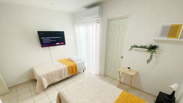 Habitació d'hotel amb dos llits, televisió, taula petita, una planta i una porta.