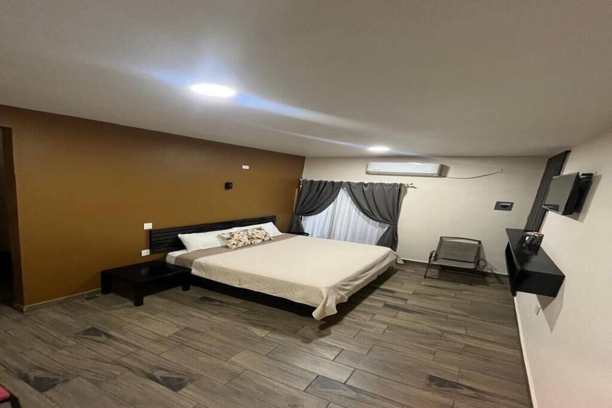 Ein Schlafzimmer mit einem Bett, Nachttischen, einem Sessel, einem Fernseher und einer Klimaanlage.