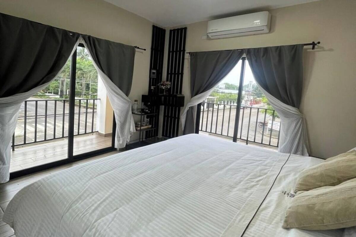 Ein Schlafzimmer mit einem großen Bett, einem Balkon mit Geländer und einer Klimaanlage an der Wand.