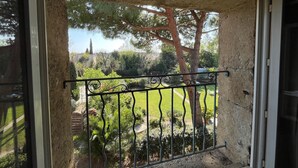 Ein Balkon mit schmiedeeisernem Geländer, einer Steinmauer und Blick auf einen Garten mit Bäumen und Rasenfläche.
