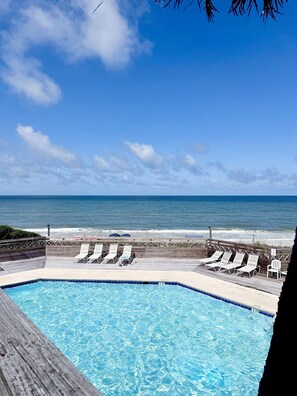 Uma piscina com água azul cristalina, um deck de madeira e vista para o oceano.