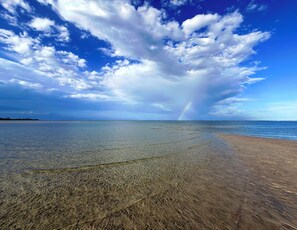 Een strand met helder water, een regenboog en een bewolkte lucht.