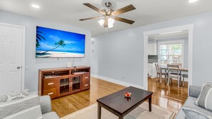 A living room with a ceiling fan, a TV, a wooden cabinet, and a dining area with chairs and a table. - Sleeps 6 | Private Patio | Near Downtown CHS (North Charleston)