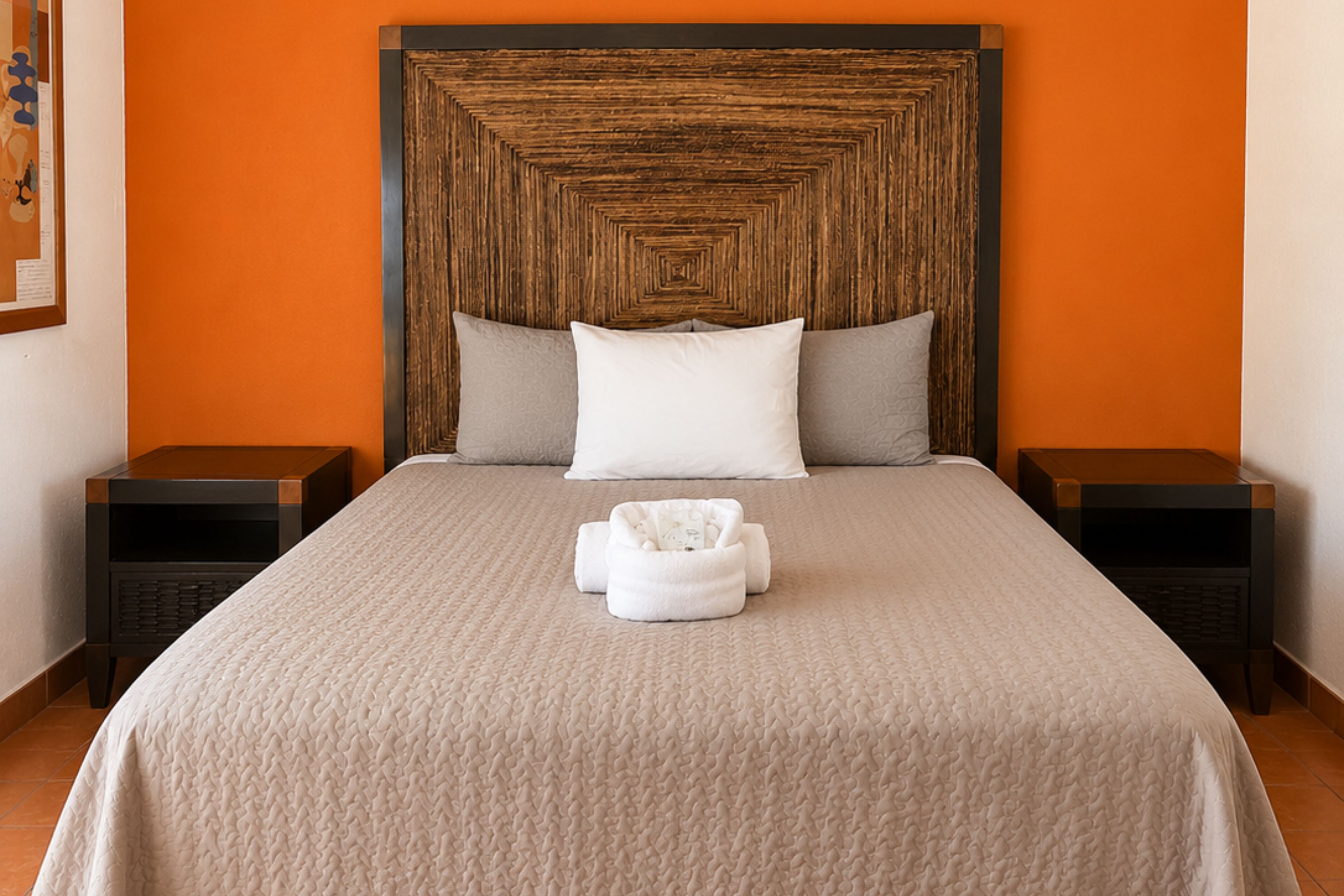 Una cama bien hecha con una colcha beige con textura, dos almohadas y una toalla blanca en el centro.