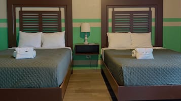 Habitación de hotel con dos camas, cada una con cabecero de madera, una mesita de noche con lámpara y una pared a rayas verdes.