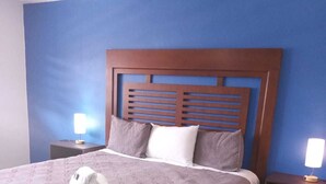 A neatly made bed with a patterned bedspread, a headboard with horizontal slats, and two bedside lamps on nightstands. - Hotel Hacienda Rosarito (Playas de Rosarito)