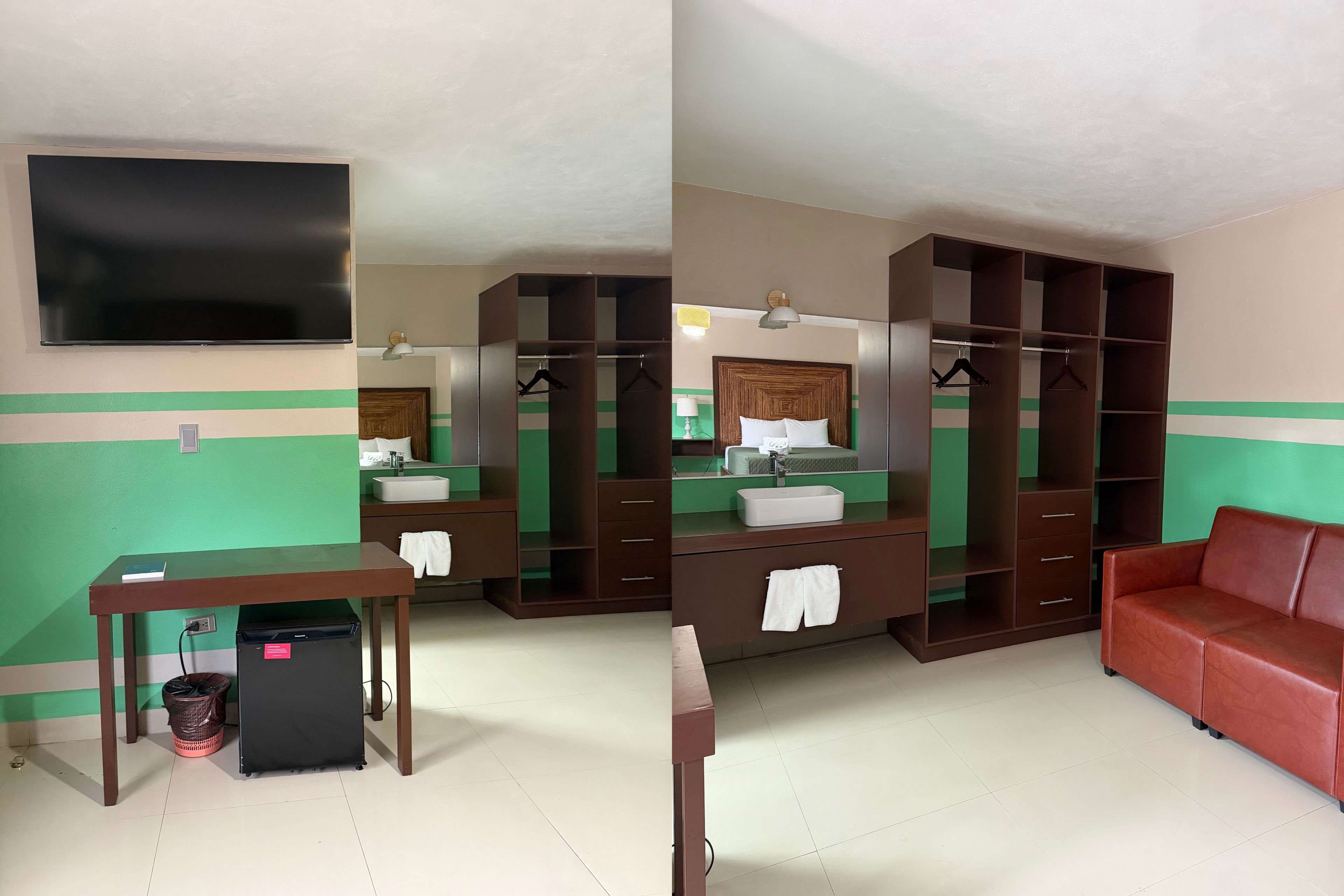 A hotel room with a flat-screen TV, a desk with a trash bin, a red sofa, a large wardrobe, and a mirror.