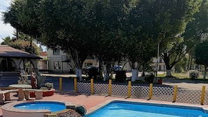A rectangular swimming pool with clear water, surrounded by a white fence and trees. - Hotel Hacienda Rosarito (Playas de Rosarito)