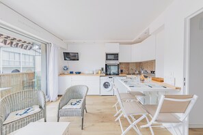 A modern kitchen with a microwave, oven, and washing machine, a dining area with chairs and a table, and a balcony with a view. - Apartment Arcachon Mouleau Plage (Arcachon)