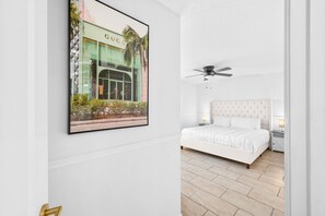 Un dormitorio con una cama, un ventilador de techo, una mesita de noche y un cuadro con una imagen de un edificio.