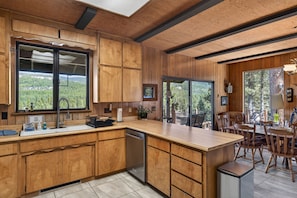A modern kitchen with wooden cabinetry, a large island, and a view of the forest. - Mountain Riverview Cliff House in The Lost Sierra (Graeagle)
