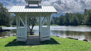 A gazebo with a wooden deck, a picnic table, and a view of a lake and forest.