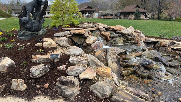 A garden with a rock waterfall, a bear statue, and a small tree.