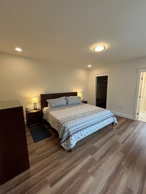 Une chambre à coucher comprenant un lit, des tables de chevet, un bureau et une porte donnant sur un placard.