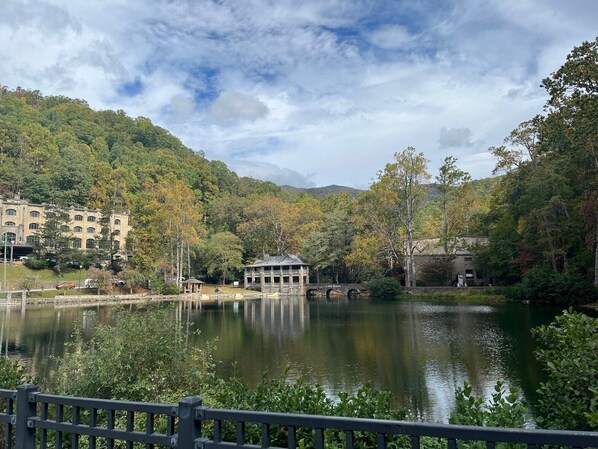 Una vista tranquila sobre un lago, con un puente, un edificio de amplias ventanas y abundante vegetación.