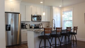 A modern kitchen with white cabinets, stainless steel appliances, a bar area with stools, and a window providing natural light.