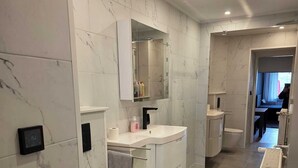 Een moderne badkamer met toilet, wastafel, spiegel en douche.